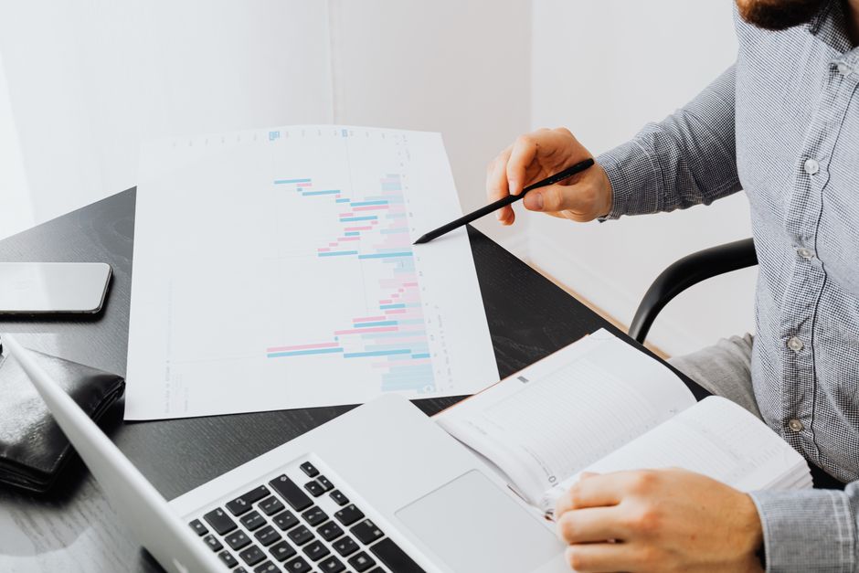 Freelancer to agency owner — An office setup with a person analyzing a graph printout while using a laptop and notebook.